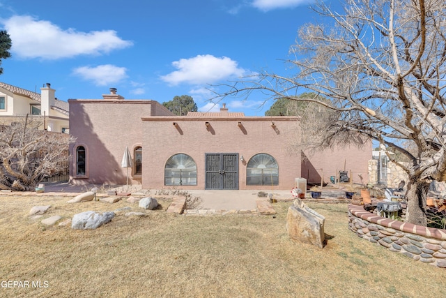 rear view of house with stucco siding, a chimney, and a lawn