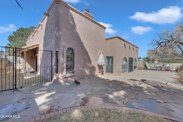 back of property with stucco siding, a patio, fence, and a gate