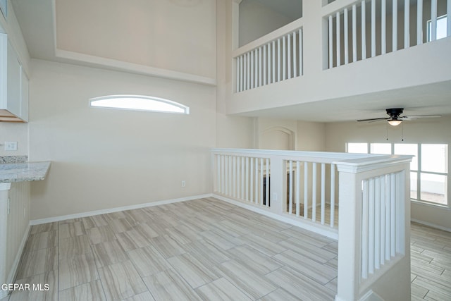 unfurnished room featuring wood tiled floor, ceiling fan, baseboards, and a towering ceiling