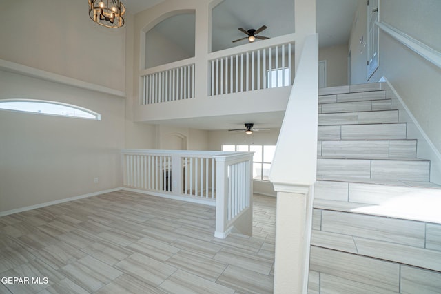 staircase with ceiling fan with notable chandelier, baseboards, and a towering ceiling