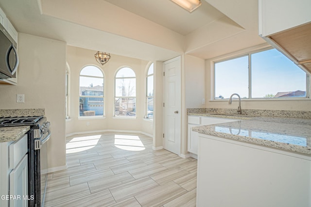 kitchen featuring a sink, white cabinetry, appliances with stainless steel finishes, baseboards, and light stone countertops