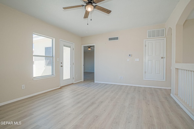 unfurnished room with arched walkways, visible vents, light wood-type flooring, and ceiling fan