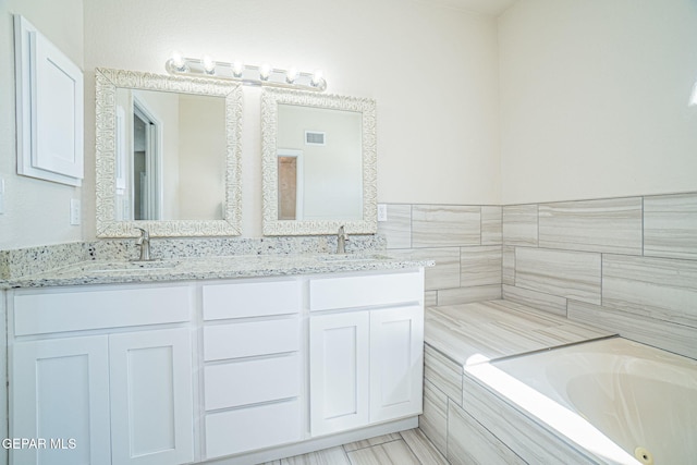 full bathroom with double vanity, visible vents, a whirlpool tub, and a sink