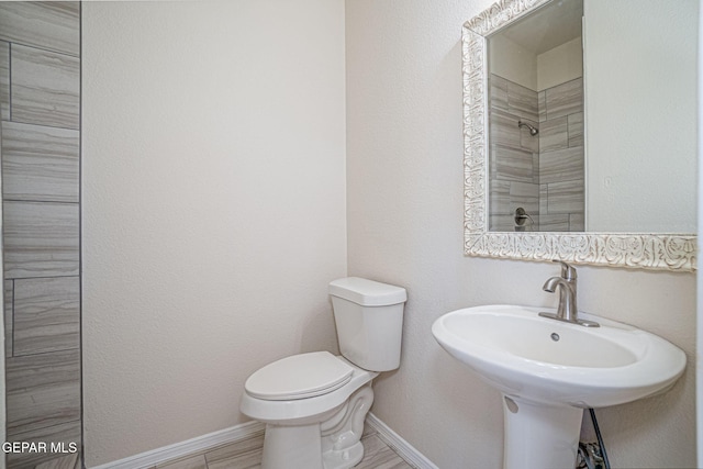 full bath featuring tiled shower, baseboards, and toilet