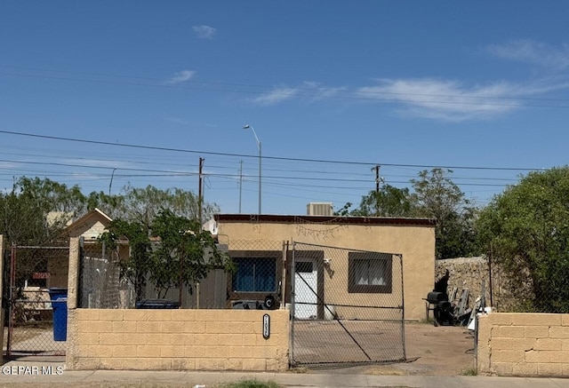 view of front facade with central air condition unit, a gate, a fenced front yard, and stucco siding