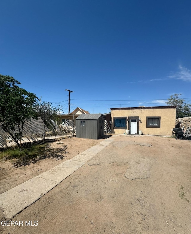 view of front of house with an outdoor structure, fence, a shed, and stucco siding