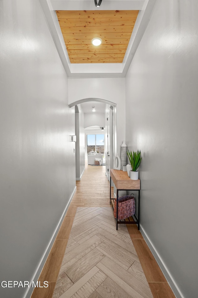 corridor featuring a tray ceiling, wood finished floors, wood ceiling, and arched walkways