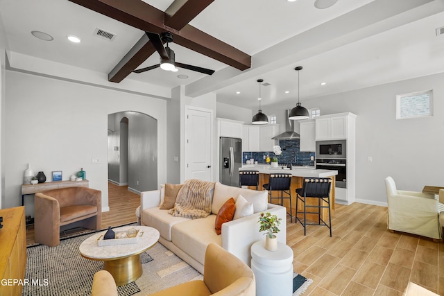 living room featuring a ceiling fan, visible vents, beam ceiling, arched walkways, and light wood-type flooring