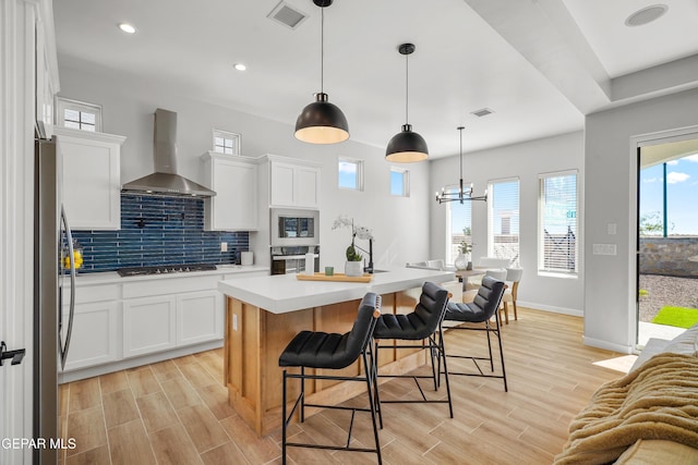 kitchen featuring visible vents, backsplash, appliances with stainless steel finishes, wall chimney exhaust hood, and wood tiled floor