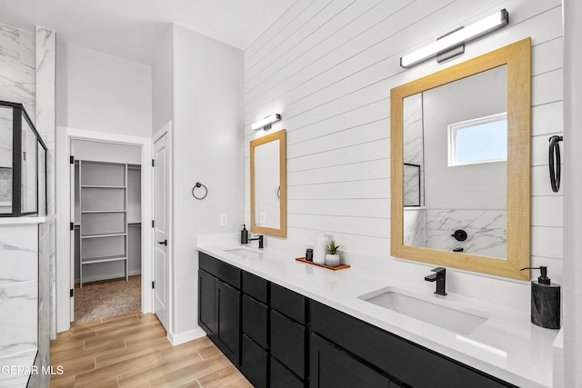 full bathroom with a sink, a marble finish shower, double vanity, and wood tiled floor