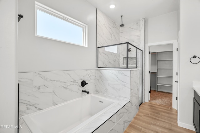 full bathroom featuring a marble finish shower, a walk in closet, wood finish floors, a bath, and vanity