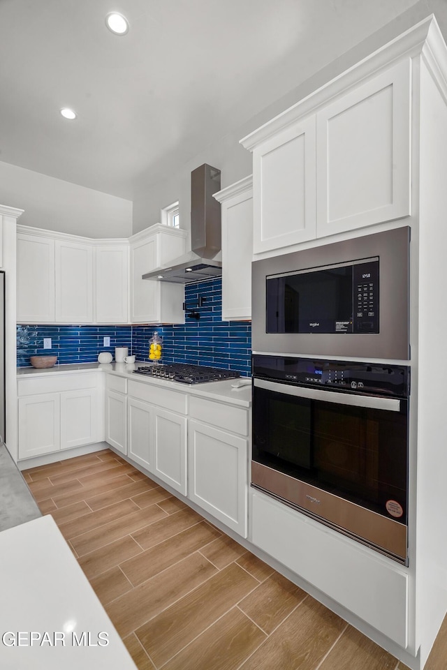 kitchen with decorative backsplash, stainless steel appliances, wall chimney exhaust hood, and wood finish floors