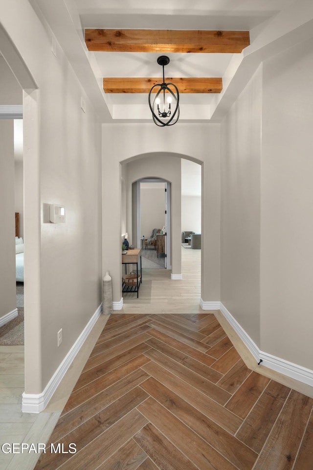 hall featuring beam ceiling, parquet floors, arched walkways, an inviting chandelier, and baseboards