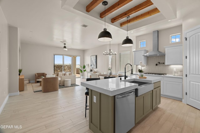 kitchen with tasteful backsplash, wall chimney range hood, light wood-style flooring, stainless steel appliances, and a sink