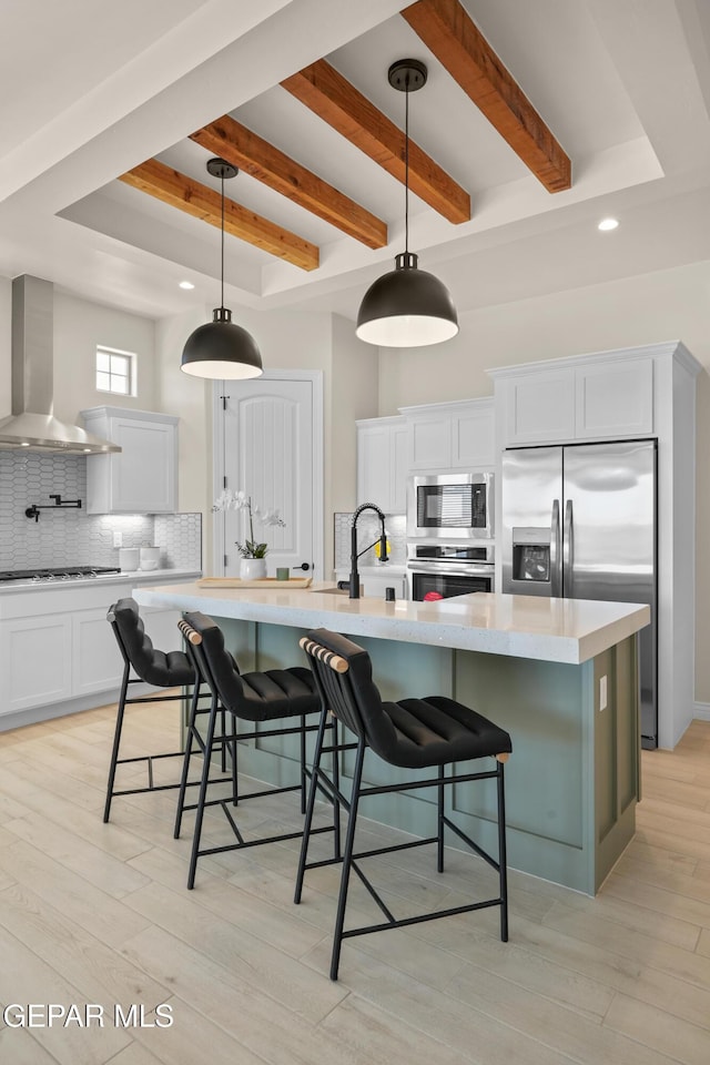 kitchen featuring a sink, wall chimney range hood, backsplash, stainless steel appliances, and light wood finished floors