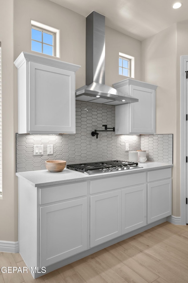 kitchen with wall chimney range hood, a healthy amount of sunlight, white cabinets, and stainless steel gas cooktop