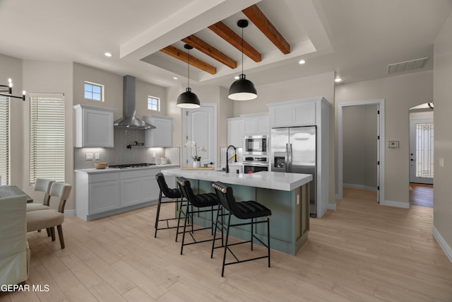 kitchen featuring visible vents, light wood finished floors, light countertops, appliances with stainless steel finishes, and wall chimney range hood