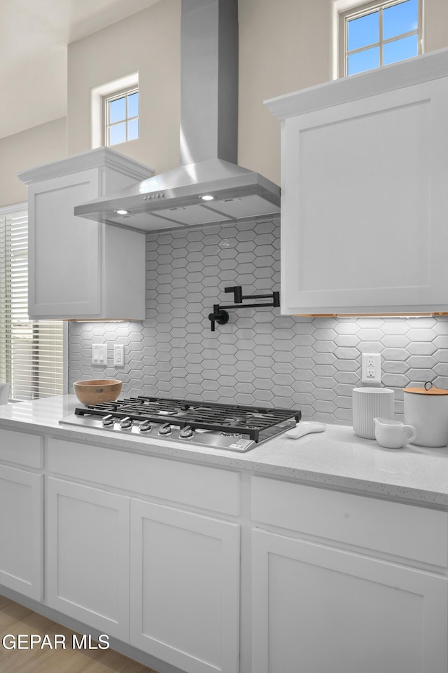 kitchen featuring decorative backsplash, white cabinets, wall chimney exhaust hood, and stainless steel gas cooktop