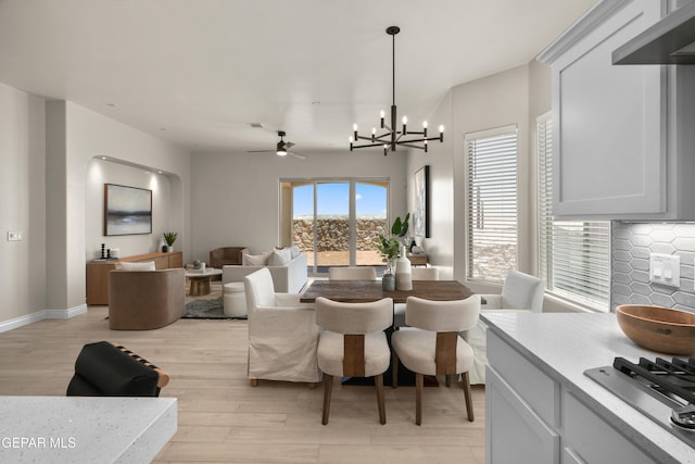 dining room featuring ceiling fan with notable chandelier, light wood-type flooring, and baseboards