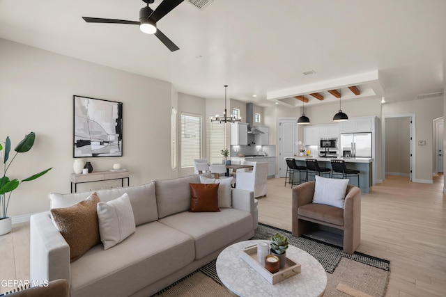 living room with light wood-style flooring, ceiling fan with notable chandelier, visible vents, and baseboards