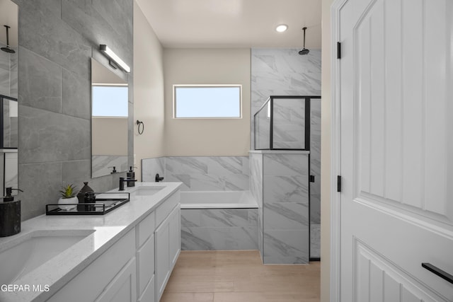 bathroom featuring a washtub, double vanity, tiled shower, tile walls, and a sink