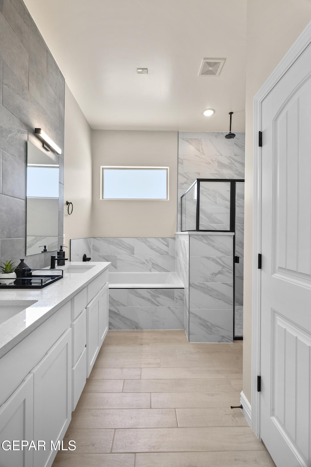 bathroom featuring visible vents, a sink, a marble finish shower, double vanity, and a bath