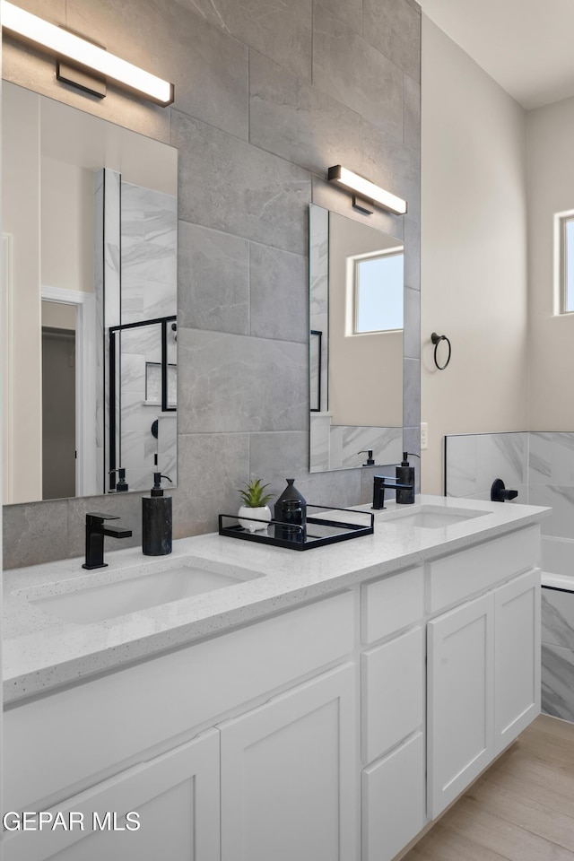 full bath with double vanity, tile walls, and a sink