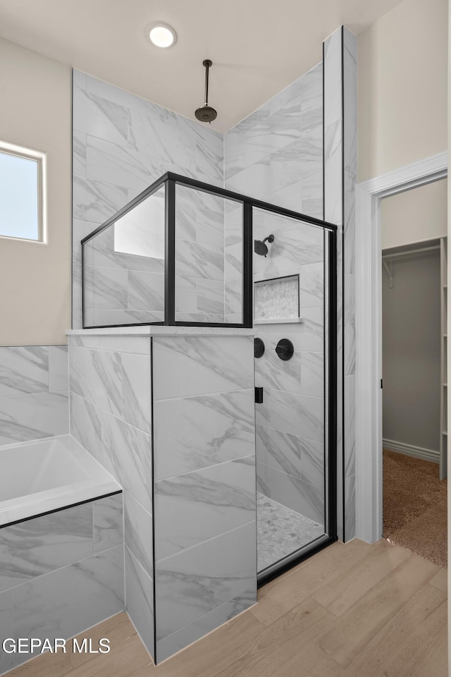 bathroom featuring a walk in closet, a tub to relax in, and a stall shower