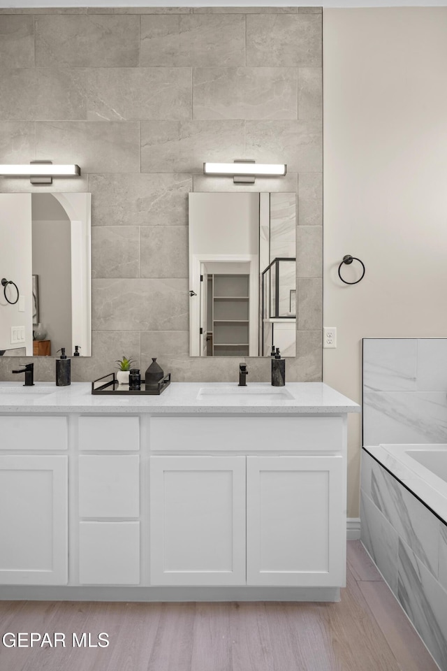 full bath with a sink, double vanity, and a washtub