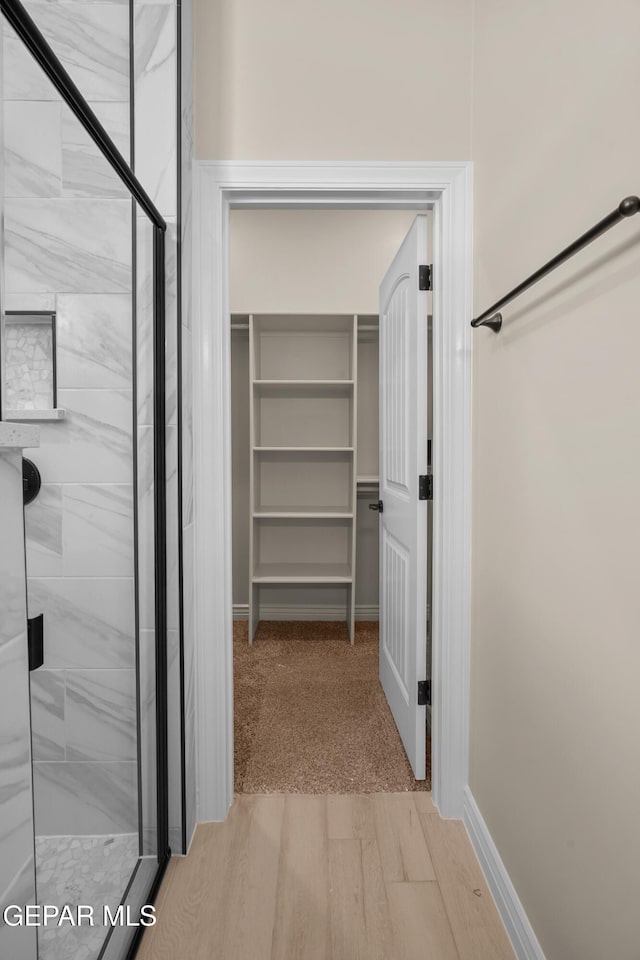 full bath featuring a stall shower, a walk in closet, and baseboards