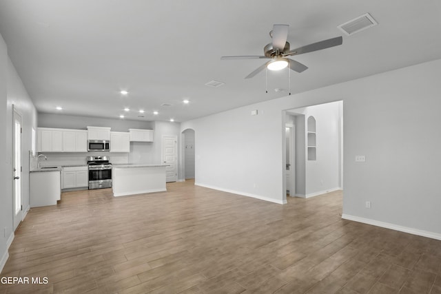 unfurnished living room featuring arched walkways, visible vents, light wood-style floors, and a sink