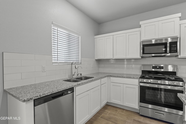 kitchen with a sink, light stone counters, stainless steel appliances, white cabinets, and wood tiled floor