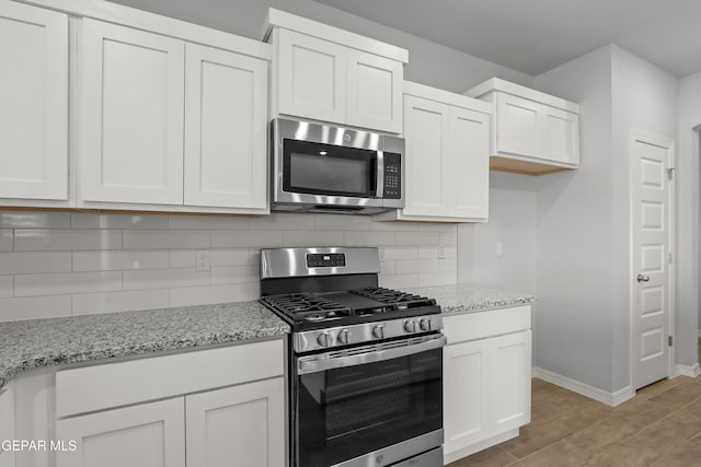 kitchen with backsplash, light stone countertops, light wood-style floors, white cabinets, and stainless steel appliances