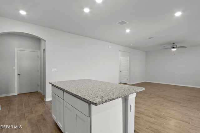 kitchen with visible vents, a kitchen island, light wood-style flooring, arched walkways, and white cabinetry