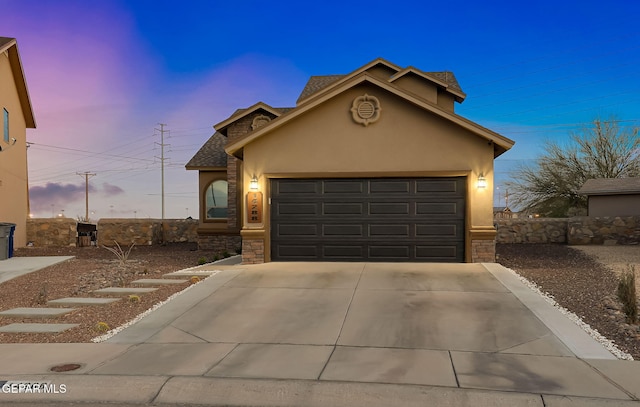 view of front facade featuring stone siding, stucco siding, an attached garage, and driveway