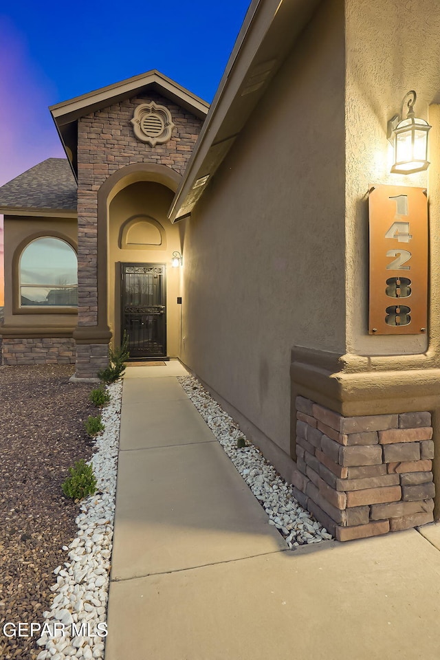 entrance to property with stone siding, roof with shingles, and stucco siding