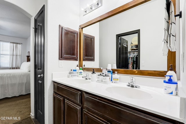 bathroom featuring double vanity, ensuite bath, a walk in closet, and a sink