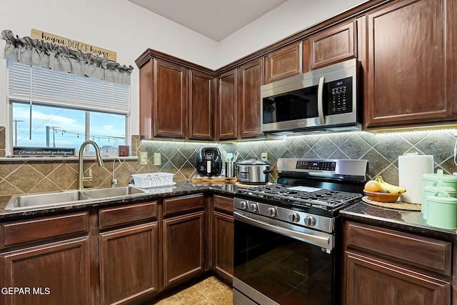 kitchen with dark stone countertops, light tile patterned flooring, a sink, appliances with stainless steel finishes, and tasteful backsplash