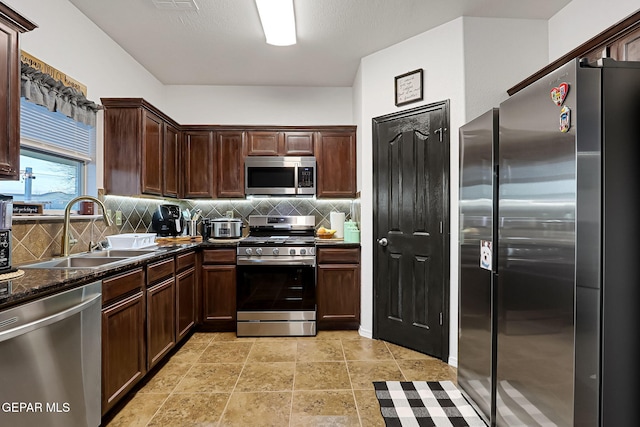 kitchen with a sink, dark stone countertops, tasteful backsplash, appliances with stainless steel finishes, and dark brown cabinets