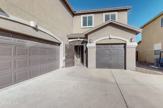 traditional home with stucco siding, driveway, an attached garage, and central AC