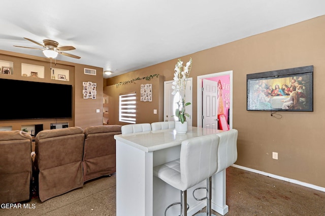 interior space with visible vents, baseboards, light countertops, a kitchen breakfast bar, and a ceiling fan