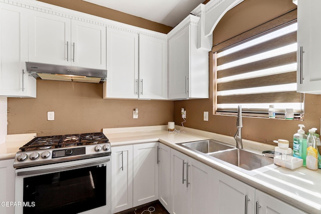 kitchen featuring under cabinet range hood, gas range, light countertops, white cabinetry, and a sink