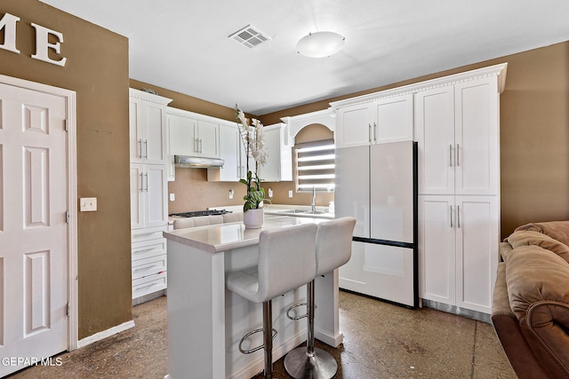 kitchen featuring under cabinet range hood, visible vents, white cabinets, and freestanding refrigerator