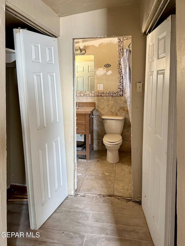 bathroom with curtained shower, toilet, tile walls, and vanity