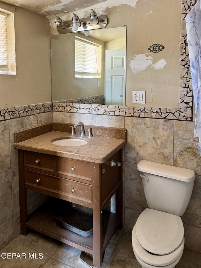 bathroom with tile patterned flooring, a wainscoted wall, toilet, vanity, and tile walls