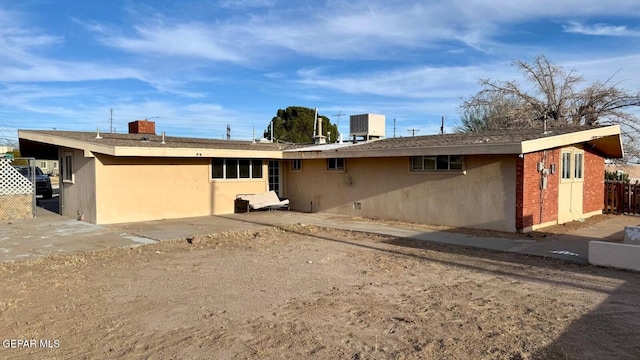 rear view of property featuring brick siding, central AC unit, fence, and stucco siding