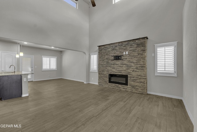 unfurnished living room with ceiling fan, a high ceiling, wood finished floors, and a fireplace