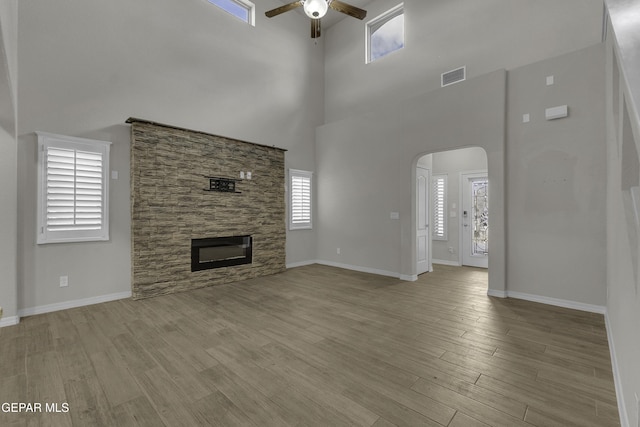 unfurnished living room featuring arched walkways, a stone fireplace, wood finished floors, and a ceiling fan