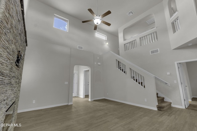 unfurnished living room with visible vents, arched walkways, wood finished floors, and stairs