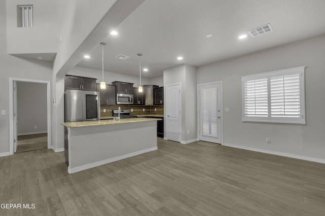 kitchen featuring visible vents, an island with sink, stainless steel appliances, light wood finished floors, and decorative backsplash